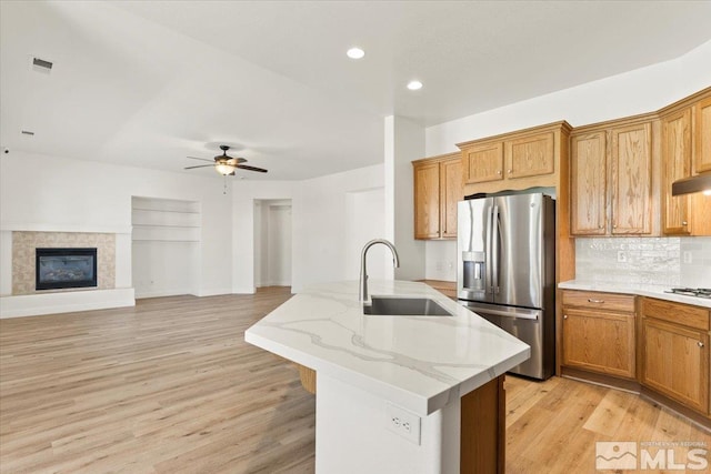 kitchen featuring appliances with stainless steel finishes, light hardwood / wood-style floors, sink, ceiling fan, and light stone counters