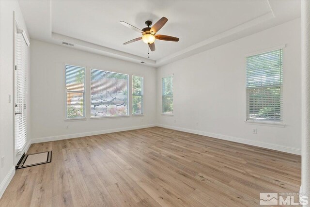 empty room featuring plenty of natural light, ceiling fan, and a tray ceiling