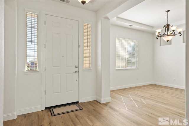 foyer featuring a notable chandelier, baseboards, a raised ceiling, and light wood-style floors