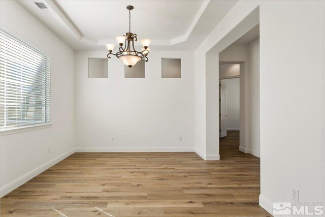 empty room featuring light wood-type flooring, a tray ceiling, and an inviting chandelier