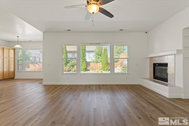 unfurnished living room featuring ceiling fan, a tile fireplace, wood finished floors, visible vents, and baseboards