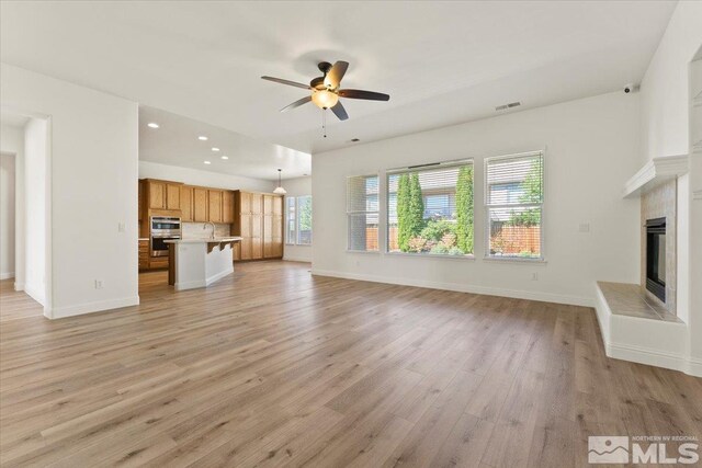 unfurnished living room featuring sink, ceiling fan, and light hardwood / wood-style floors