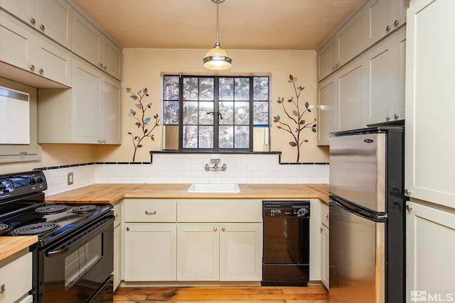 kitchen with pendant lighting, light hardwood / wood-style flooring, butcher block counters, black appliances, and sink