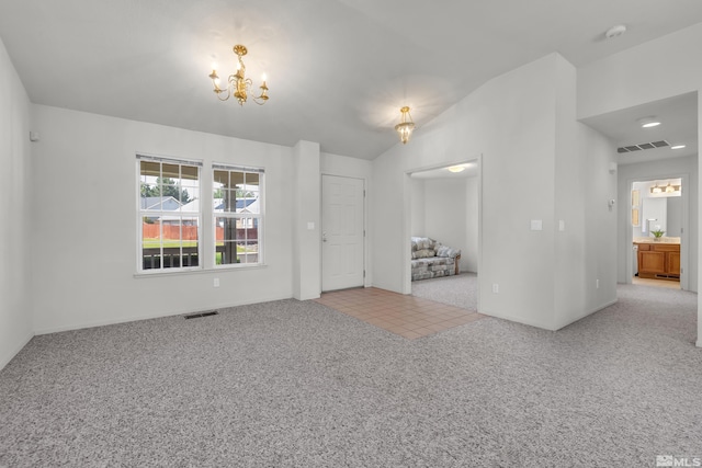 carpeted empty room with tile patterned flooring, visible vents, vaulted ceiling, and a notable chandelier