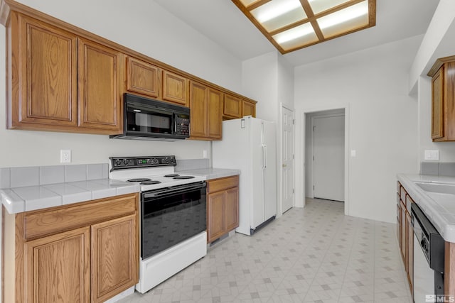 kitchen featuring brown cabinetry, tile counters, white appliances, and light floors