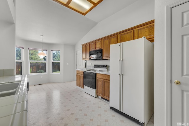 kitchen with black microwave, range with electric stovetop, tile counters, freestanding refrigerator, and brown cabinetry