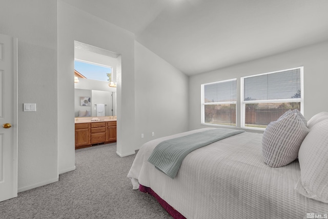 bedroom with light colored carpet, vaulted ceiling, ensuite bath, and baseboards