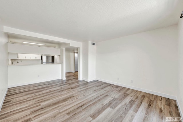 unfurnished living room with light wood-type flooring and a textured ceiling