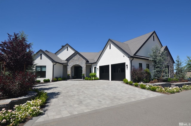 view of front of house with a garage, stone siding, decorative driveway, and stucco siding