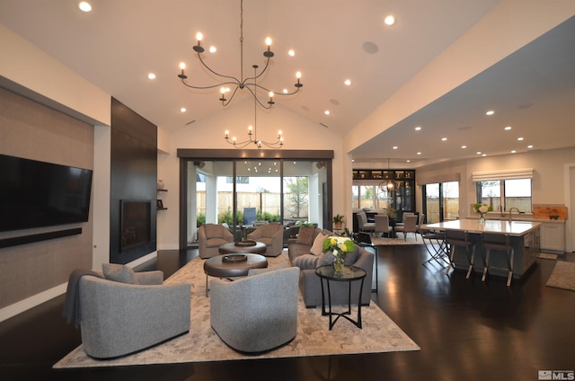 living room featuring dark wood-type flooring, vaulted ceiling, a notable chandelier, and plenty of natural light