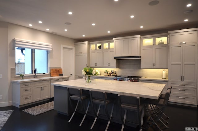 kitchen featuring light stone counters, under cabinet range hood, a sink, range, and a center island