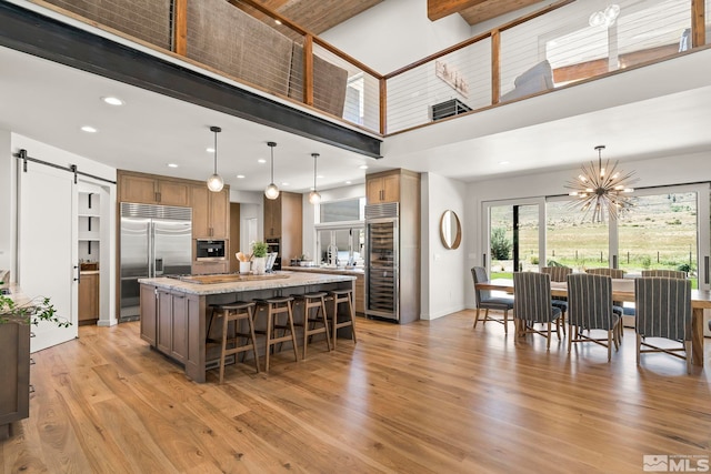 kitchen with light hardwood / wood-style floors, a center island, stainless steel appliances, a barn door, and a towering ceiling