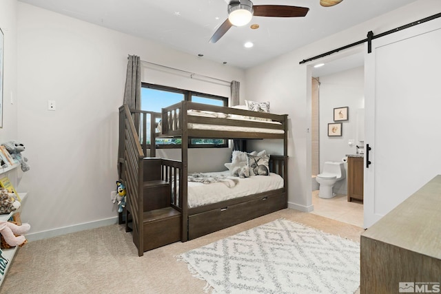 tiled bedroom featuring a barn door, ceiling fan, and connected bathroom