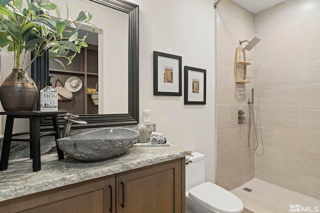 bathroom with toilet, a tile shower, and vanity