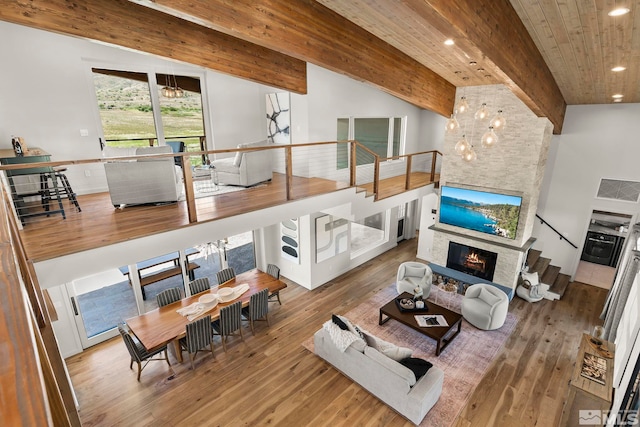 living room with hardwood / wood-style floors, an inviting chandelier, beamed ceiling, and a stone fireplace