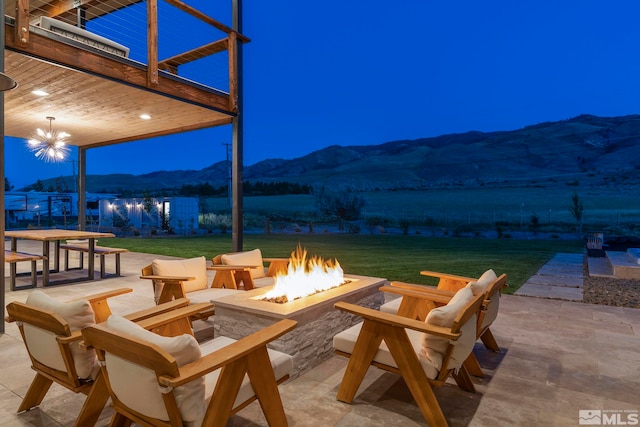 patio at night featuring a mountain view, a fire pit, and a yard