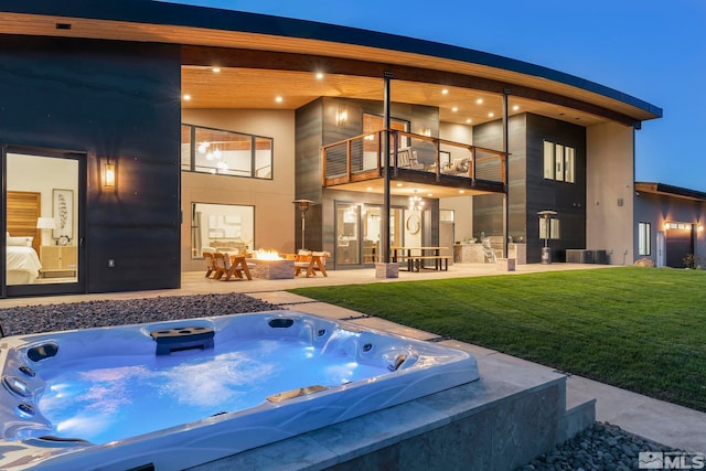 back house at night featuring a yard, a patio, a balcony, and a hot tub