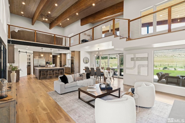 living room featuring beamed ceiling, light hardwood / wood-style flooring, a notable chandelier, a barn door, and a towering ceiling