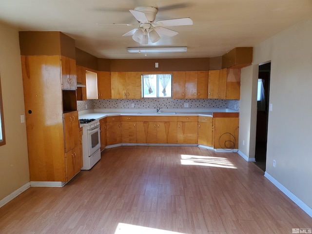 kitchen featuring light wood-type flooring, sink, white range with gas cooktop, ceiling fan, and tasteful backsplash