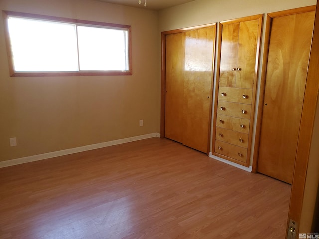 unfurnished bedroom with two closets, multiple windows, and light hardwood / wood-style flooring