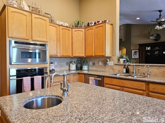 kitchen with backsplash, appliances with stainless steel finishes, sink, ceiling fan, and light stone counters