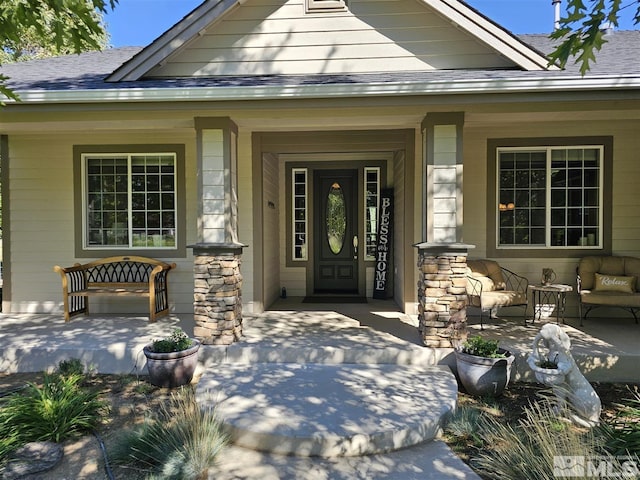 view of exterior entry featuring covered porch, a shingled roof, and stone siding