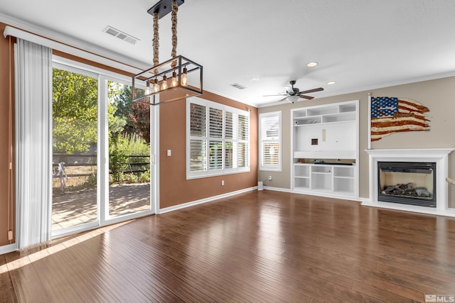 unfurnished living room with ornamental molding, dark hardwood / wood-style floors, ceiling fan with notable chandelier, and built in shelves