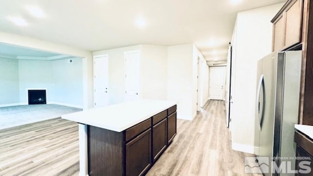 kitchen with light wood-type flooring, a center island, stainless steel refrigerator, and dark brown cabinets