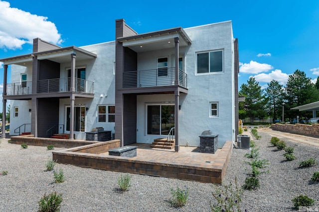 back of property with central AC unit, a patio area, and a balcony