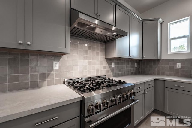 kitchen featuring tasteful backsplash, high end range, light countertops, gray cabinetry, and under cabinet range hood