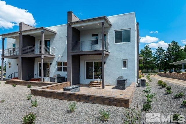 back of property with cooling unit, a patio area, a balcony, and stucco siding