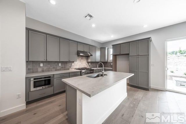 kitchen featuring decorative backsplash, gray cabinets, a sink, and under cabinet range hood