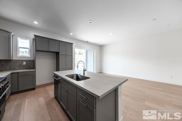 kitchen with black dishwasher, a sink, light wood-style flooring, and decorative backsplash