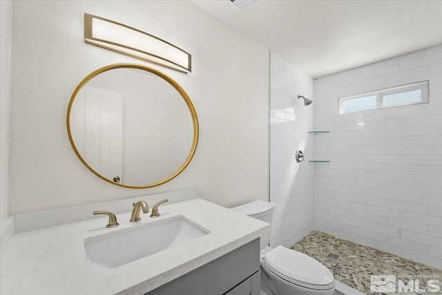 bathroom featuring vanity, toilet, tiled shower, and a textured ceiling