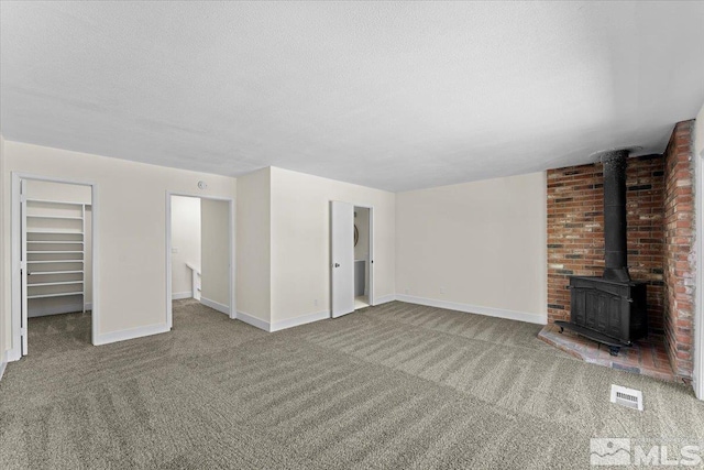 unfurnished living room featuring a wood stove, light colored carpet, and a textured ceiling