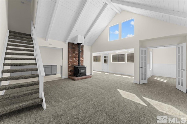 unfurnished living room with a wood stove, carpet floors, beam ceiling, french doors, and high vaulted ceiling