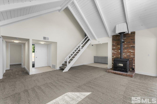 unfurnished living room with a wood stove, carpet, and beamed ceiling