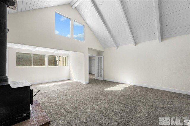 unfurnished living room with high vaulted ceiling, a wood stove, beamed ceiling, and carpet floors