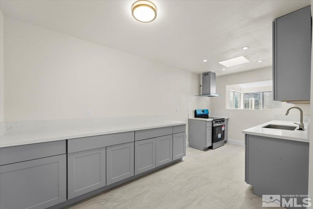 kitchen featuring gray cabinets, a skylight, sink, electric range, and wall chimney exhaust hood