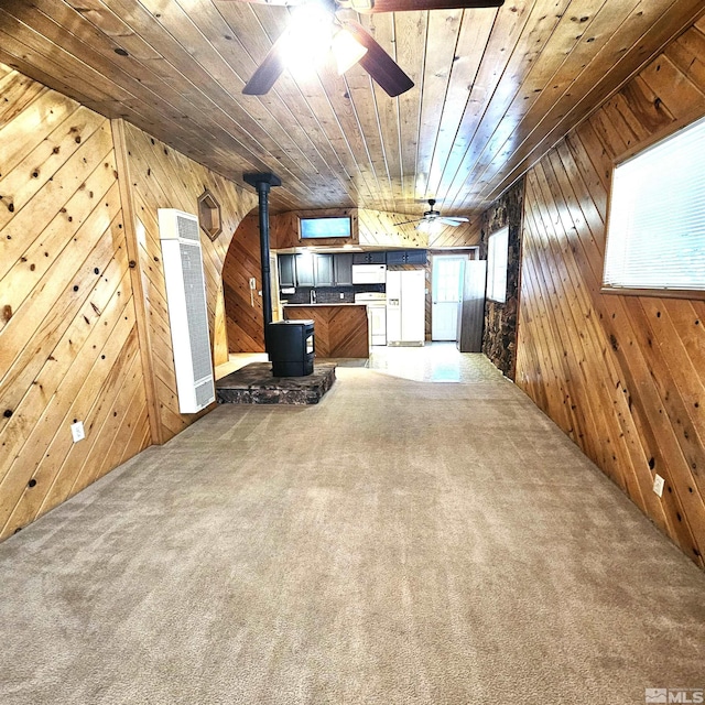 unfurnished living room featuring carpet flooring, a wood stove, and wooden walls