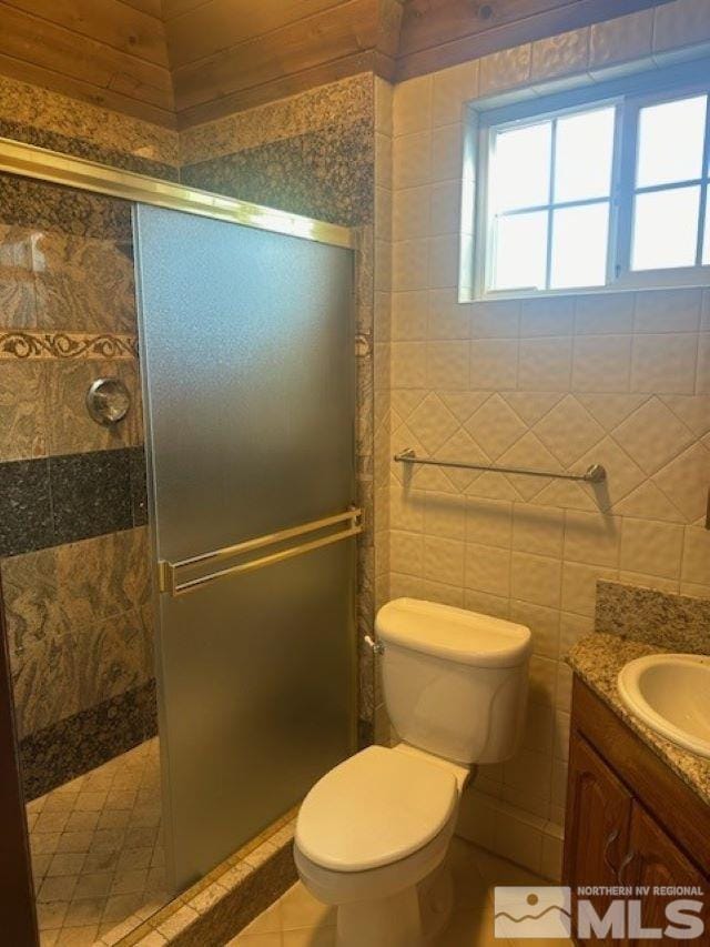 bathroom featuring toilet, tile walls, a stall shower, and vanity