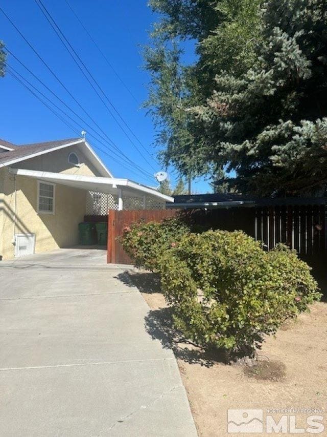 view of property exterior featuring an attached carport, driveway, and fence