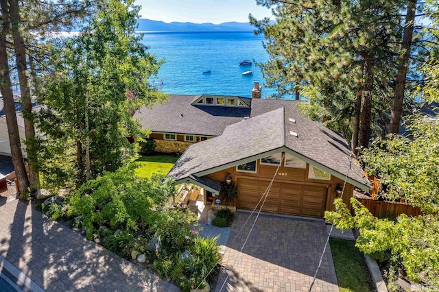 view of front facade featuring decorative driveway, a shingled roof, an attached garage, a water and mountain view, and fence