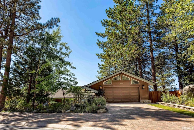 view of front of house featuring decorative driveway, an attached garage, and fence