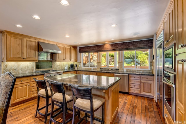 kitchen featuring appliances with stainless steel finishes, a kitchen breakfast bar, light wood finished floors, and wall chimney exhaust hood