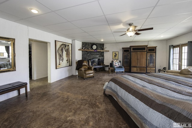 bedroom featuring a stone fireplace, a paneled ceiling, concrete floors, and ceiling fan