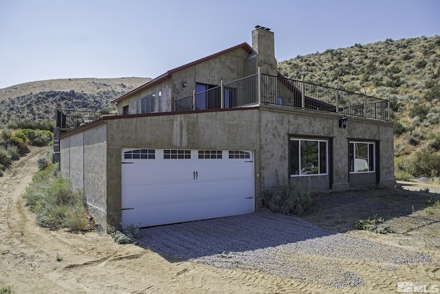 view of side of property featuring a balcony, stucco siding, gravel driveway, and a garage