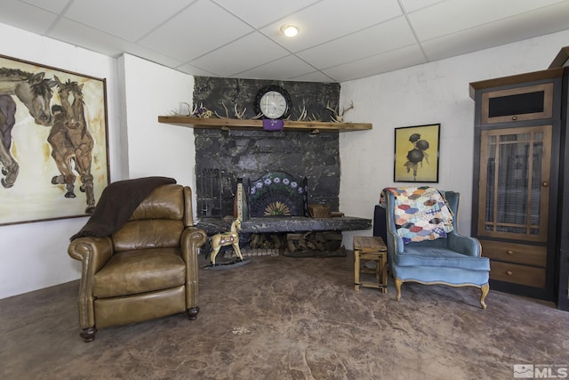 sitting room featuring a drop ceiling and a stone fireplace