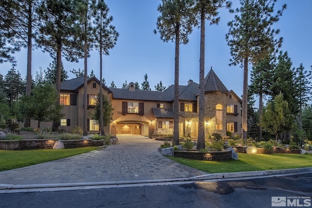 view of front of house with stone siding, decorative driveway, stucco siding, a front lawn, and a chimney