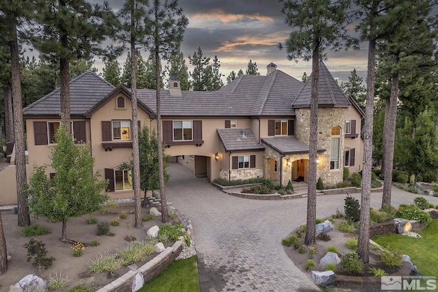 view of front of home featuring stone siding, decorative driveway, a chimney, and stucco siding